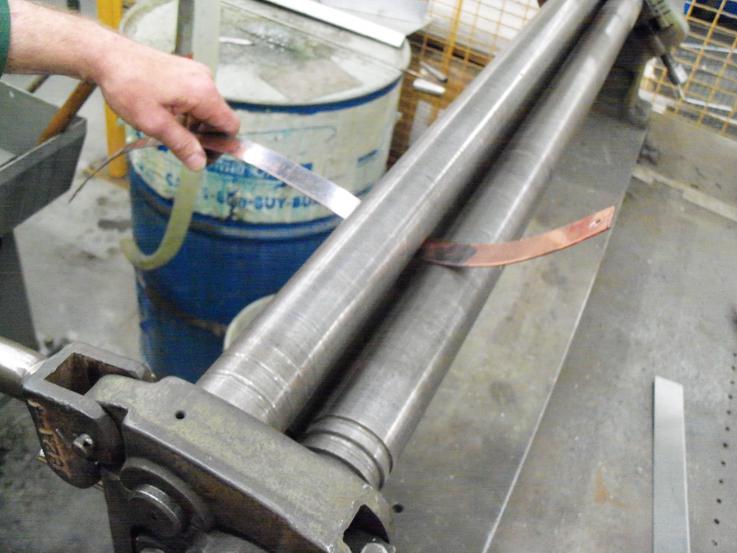 Hand shaping the copper luggage straps through a rolling press.